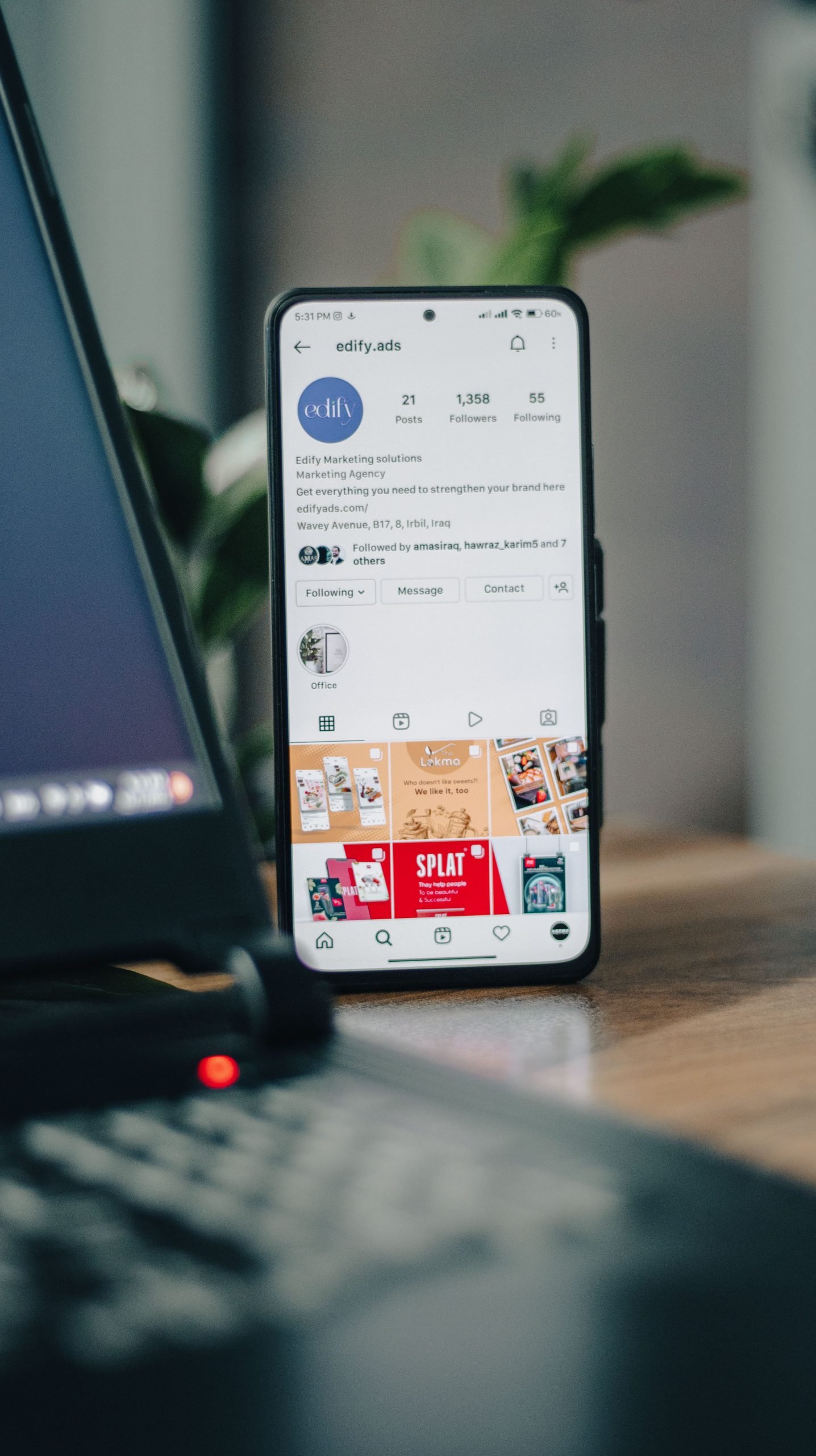 Vertical shot of a smartphone displaying an Instagram profile next to a laptop, representing social media engagement.